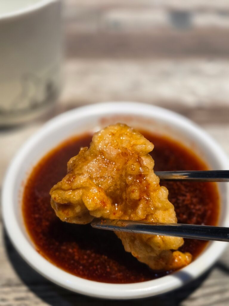 A piece of crispy tangsuyuk dipped in sweet and sour sauce